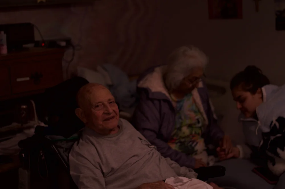 A group gathered around a seated person in a warmly lit living room.