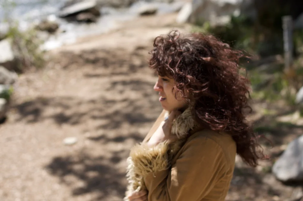 A curly-haired person in profile in a sunlit outdoor setting.